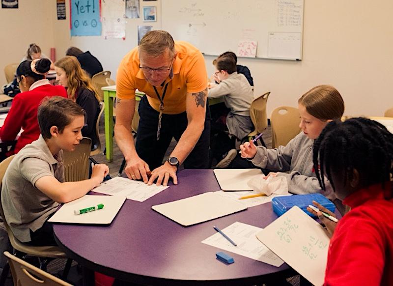 Middle school math teacher Donald Eldridge works with 3 Parker Performing Arts students in an academic classroom, reviewing work they’re doing while seated at a table.