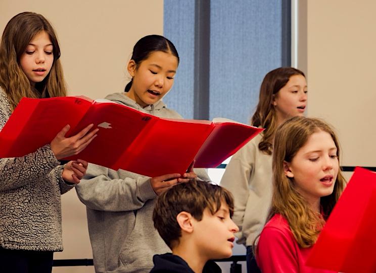 Parker Performing Arts School students rehearse in a vocal music class.  They’re holding sheet music in folders.